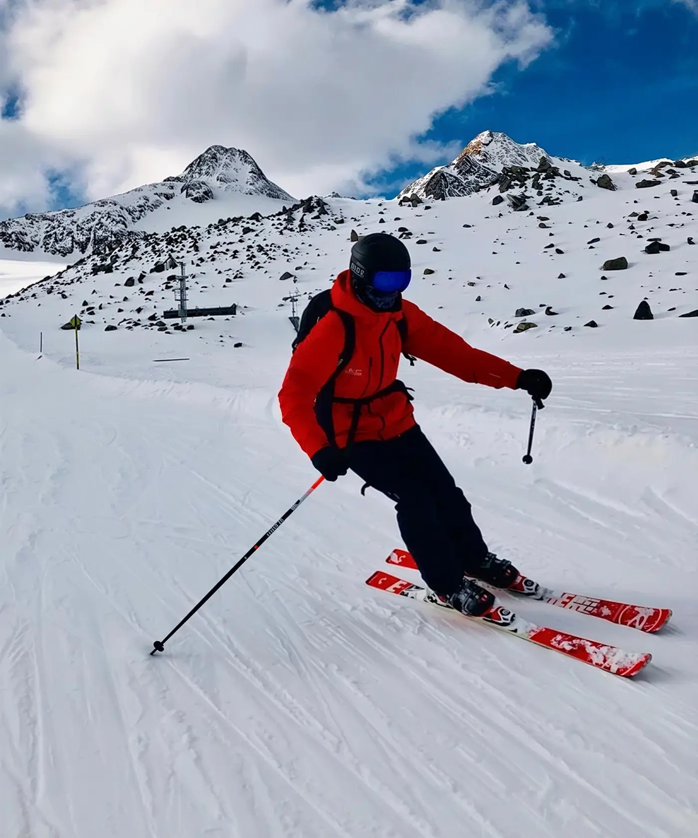 Skiër in een rode jas maakt een bocht op een zonnige piste